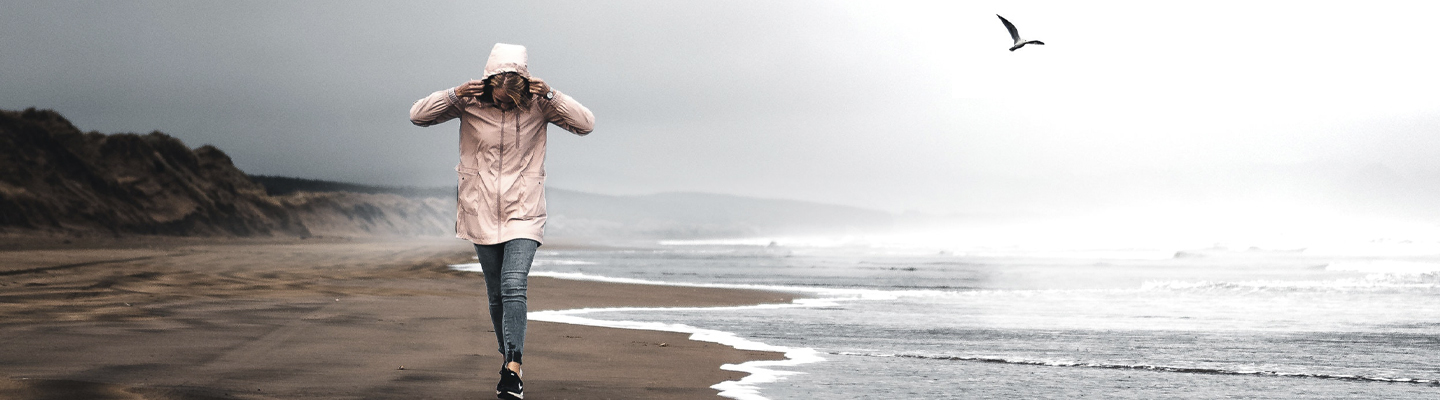 Frau spaziert bei stürmischen Wetter an der Küste