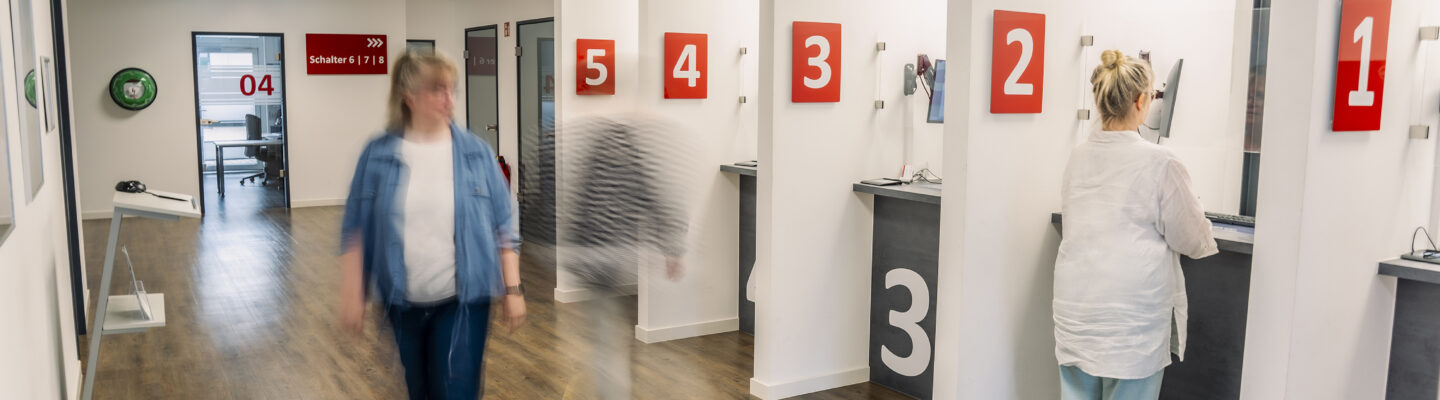 Eingangbereich der Straßenverkehrsabteilung, Bürgerin am Schalter, zwei Personen in Bewegung