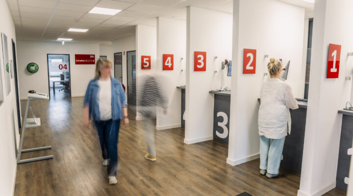 Eingangbereich der Straßenverkehrsabteilung, Bürgerin am Schalter, zwei Personen in Bewegung