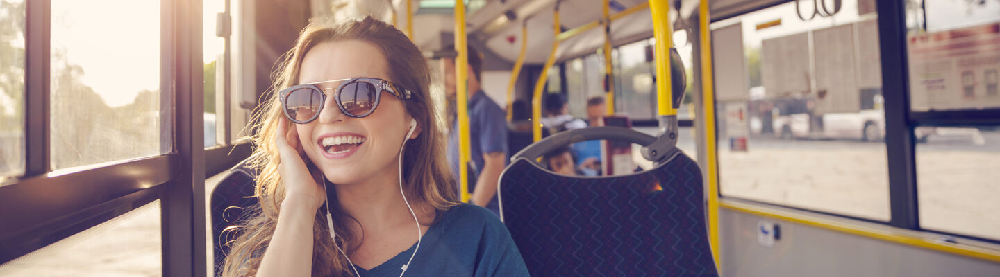 Glückliche Frau sitzt im Bus und telefoniert über Kopfhörer