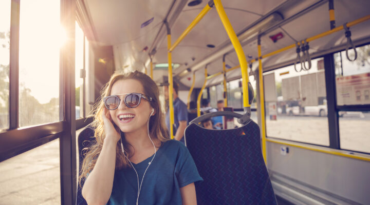 Glückliche Frau sitzt im Bus und telefoniert über Kopfhörer