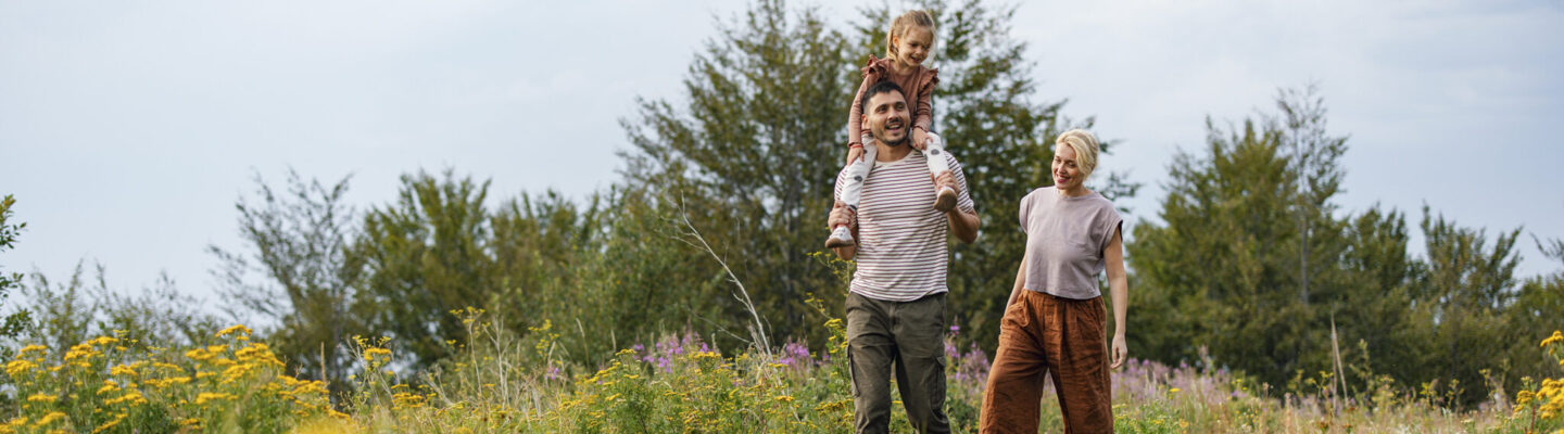 Glückliche Familie spaziert an einem sonnigen Tag durch eine lebendige Wiese.