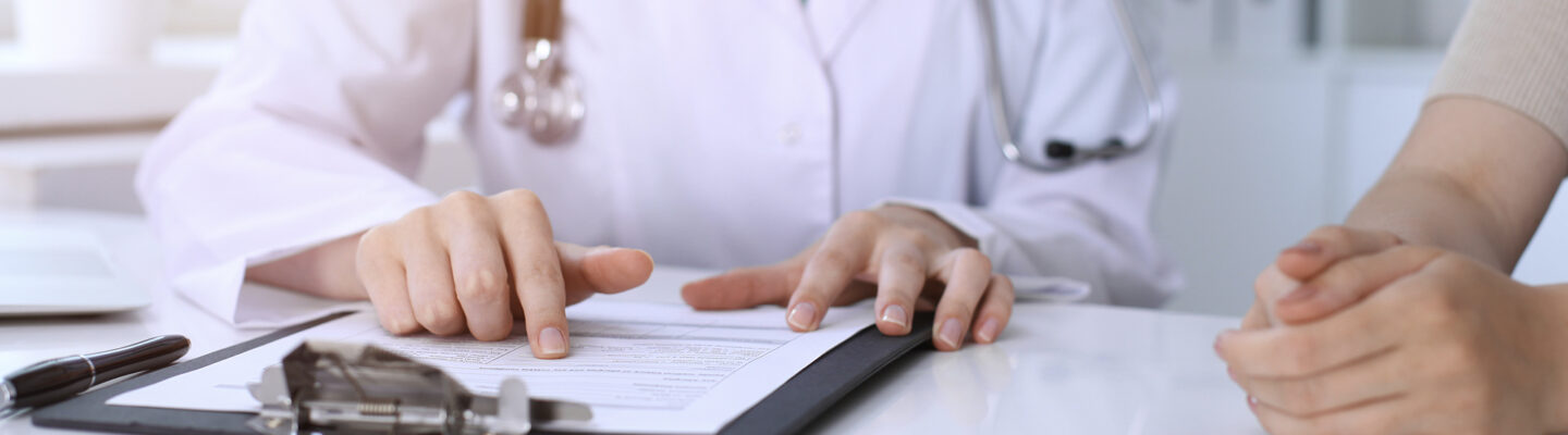 Beratungsgespräch zwischen einer Ärztin und Patient. Die Ärztin zeigt auf ein Schriftstück.