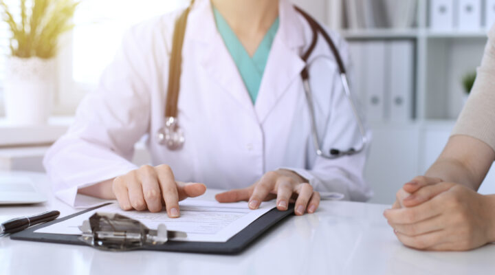 Beratungsgespräch zwischen einer Ärztin und Patient. Die Ärztin zeigt auf ein Schriftstück.