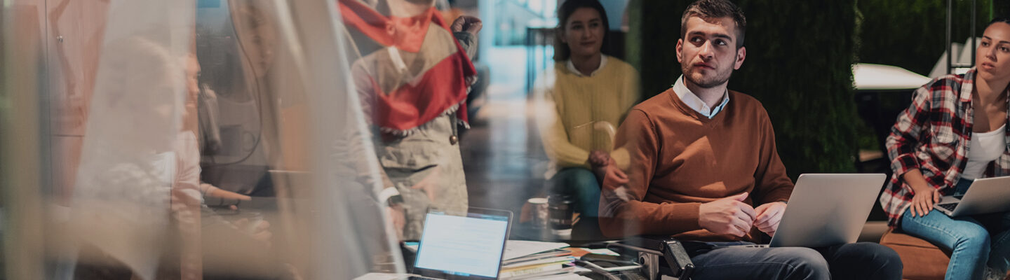 Eine Geschäftsfrau präsentiert ein Projekt vor einem jungen, vielfältigen Team von Menschen in einem modernen Büro