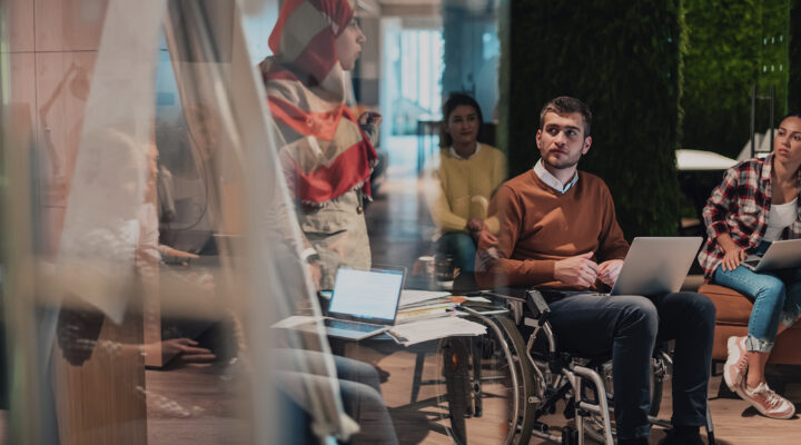 Eine Geschäftsfrau präsentiert ein Projekt vor einem jungen, vielfältigen Team von Menschen in einem modernen Büro