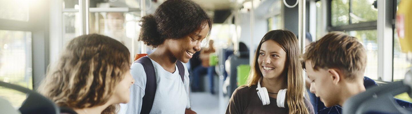 Fröhliche Schüler nutzen ihr Handy während der Busfahrt zur Schule.