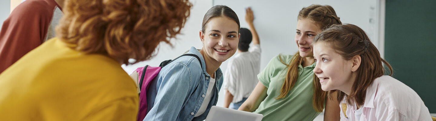 Jugendliche Schüler unterhalten sich und lachen in einem lebendigen Klassenzimmer während der Schulanfangszeit.