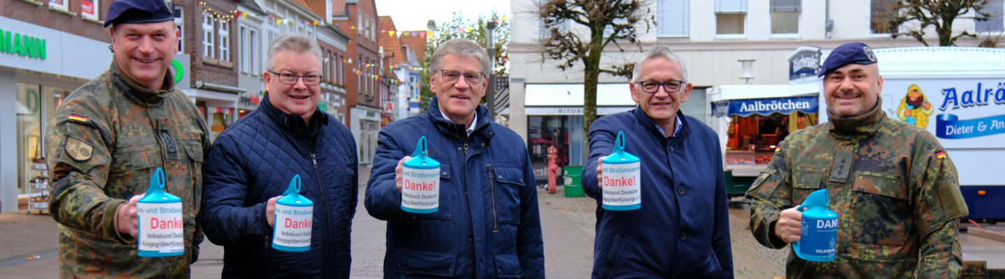 Fünf Männer stehen in einer Einkaufsstraße und halten jeweils eine Sammeldose mit der Aufschrift ‚Danke!‘ in der Hand. Zwei der Männer tragen Bundeswehruniformen, die drei anderen dunkle Jacken. Im Hintergrund sind Geschäfte und ein Brötchenwagen zu sehen.