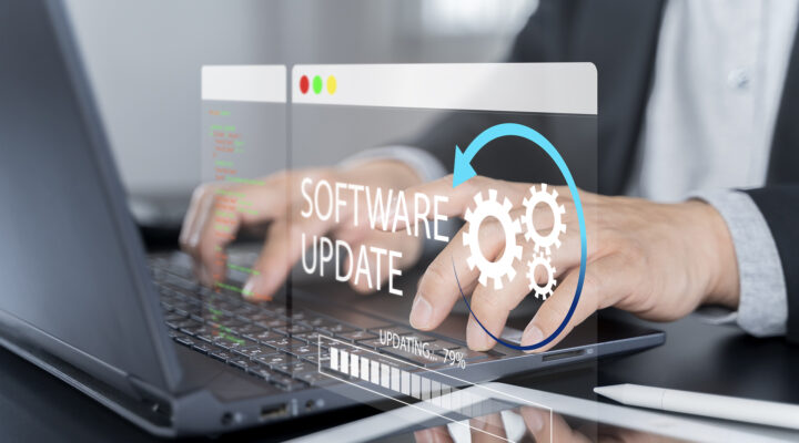Eine Person arbeitet an einem Laptop. Über dem Bild ist eine grafische Einblendung mit der Aufschrift ‚Software Update‘, Zahnradsymbolen und einem Fortschrittsbalken zu sehen – Symbol für eine laufende Systemaktualisierung.